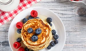 Pfannkuchenstapel mit frischen Heidelbeeren, Himbeeren und Honig, Milch und frischen Beeren, gesundes Frühstückskonzept, Draufsicht